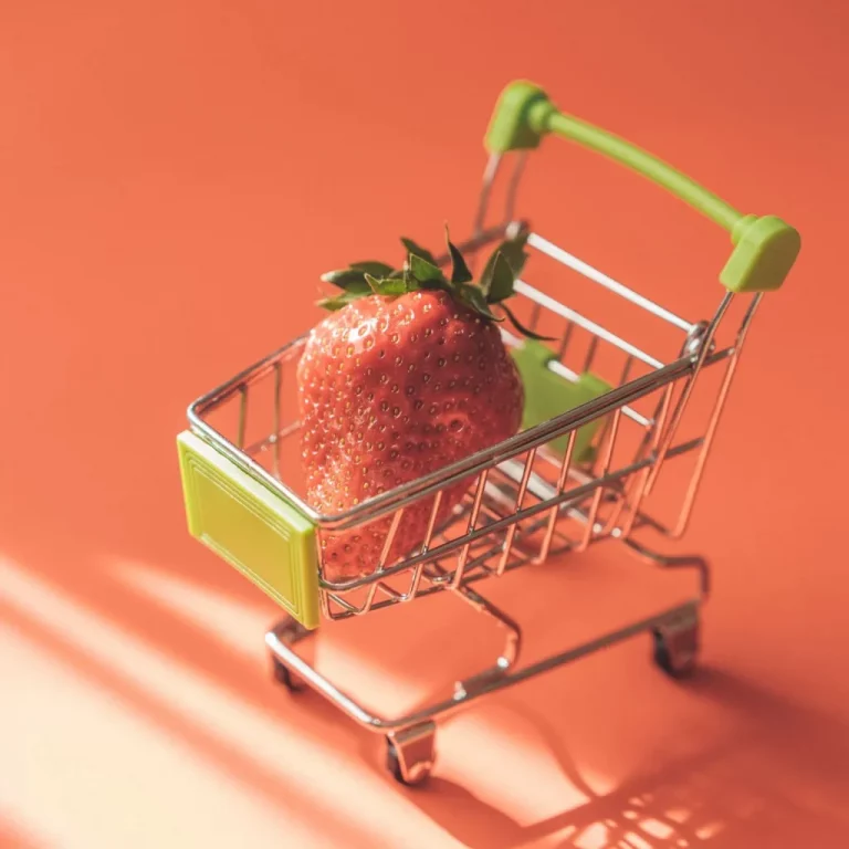 Feature image for how to save money grocery shopping post features a Shopping cart with a strawberry in it