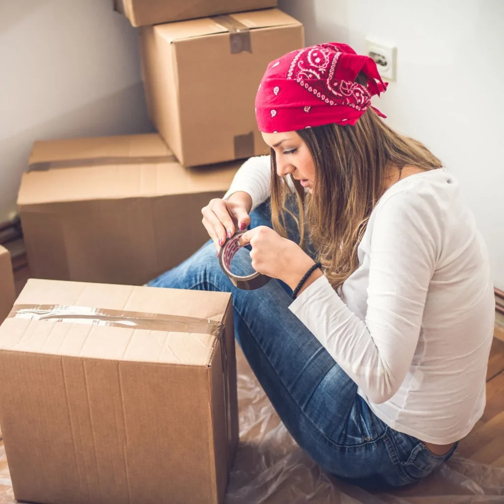 Woman taping boxes - cover image for tips for moving out for the first time blog post