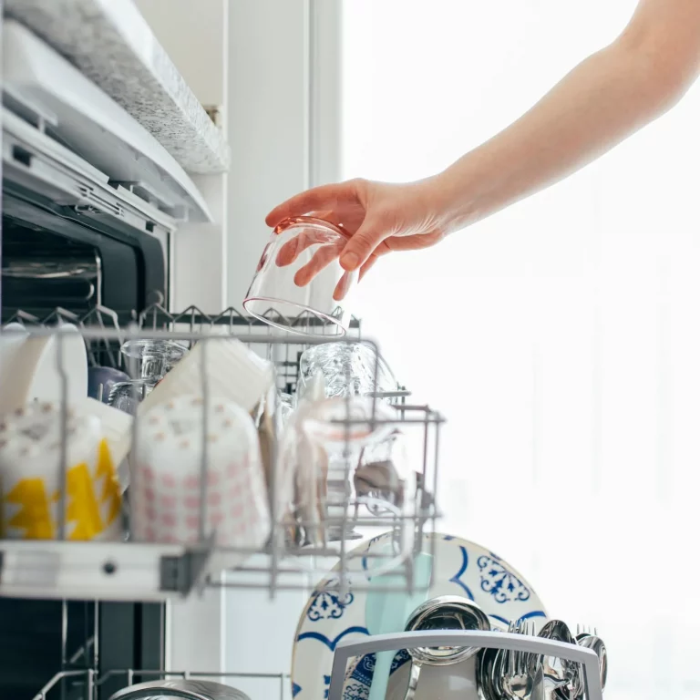 Hand placing a cup into a dishwasher